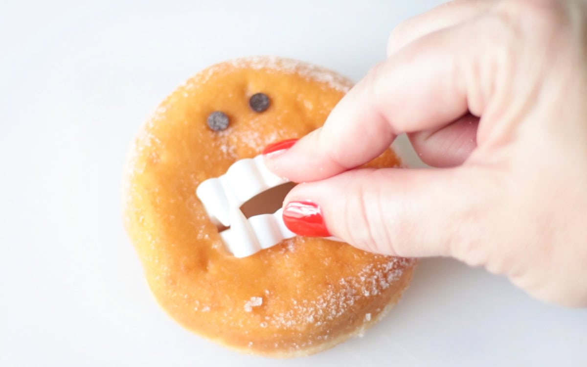 Hand placing vampire fangs inside donut hole.