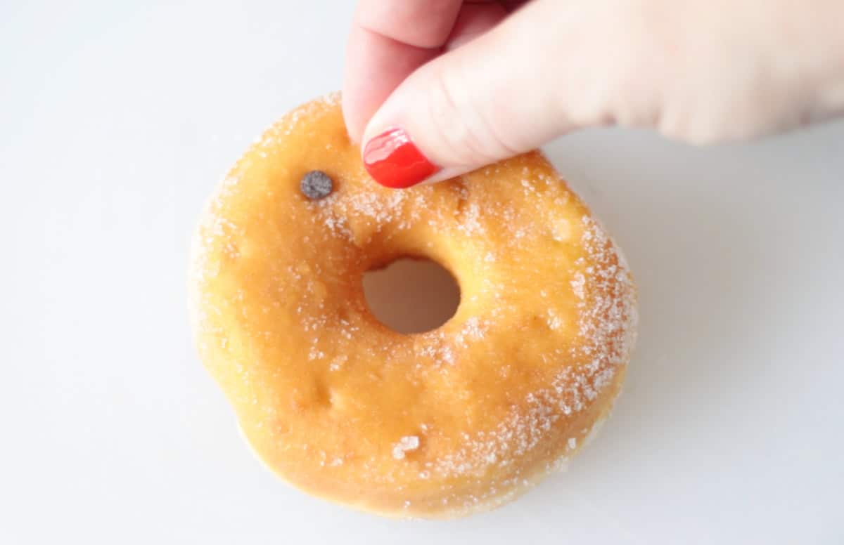 Hand placing two chocolate chips on donut.