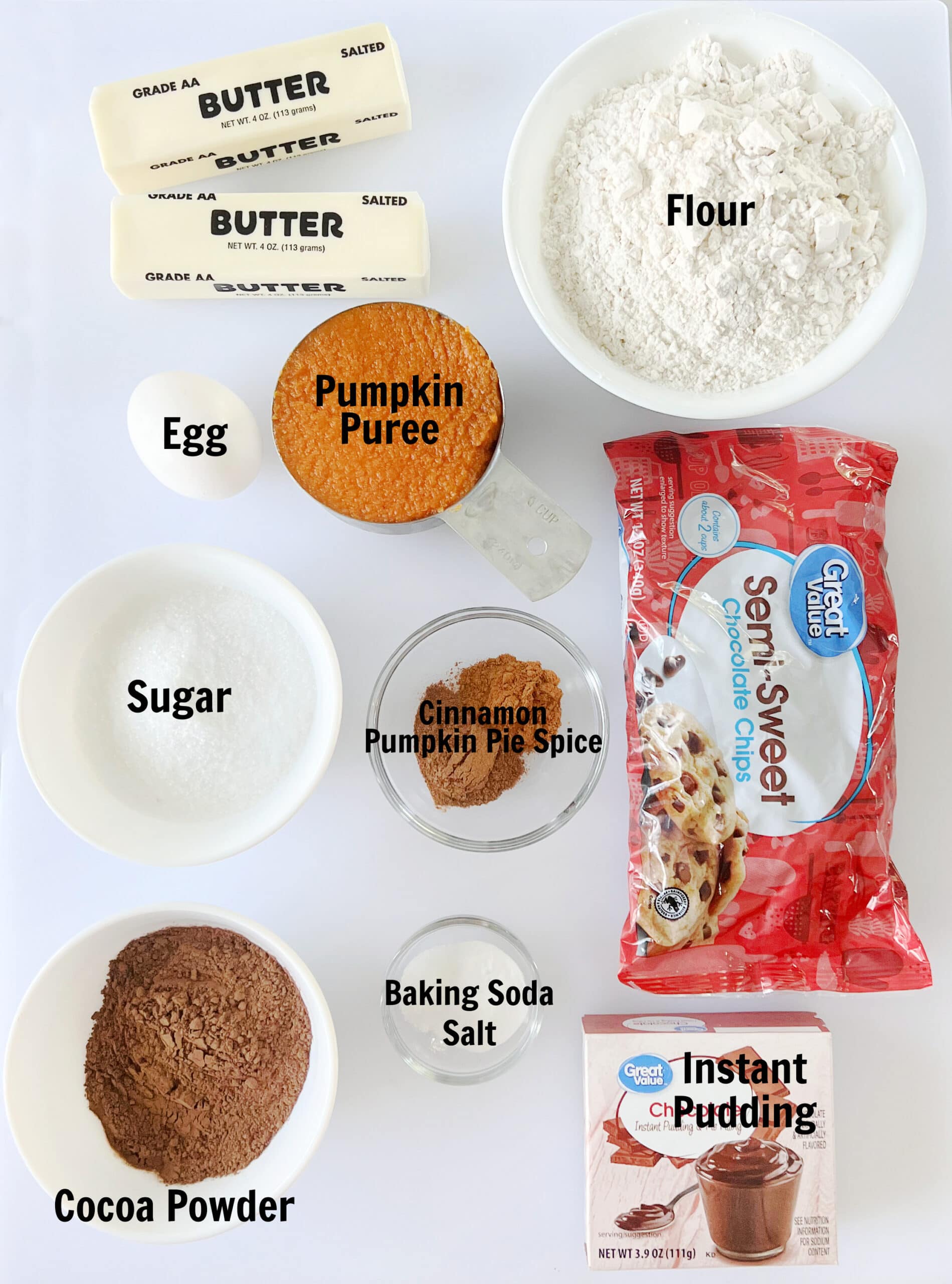 Bowls of flour, sugar, baking soda and salt, two sticks of butter, an egg, cup of pumpkin puree, bowl of baking cocoa, box of chocolate pudding and bag of chocolate chips.