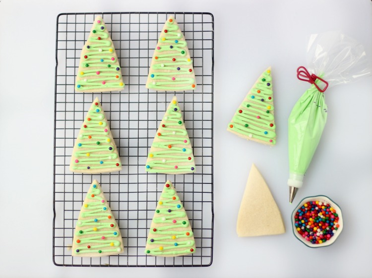 tree sugar cookies on baking rack with bowl of sprinkles and icing tube