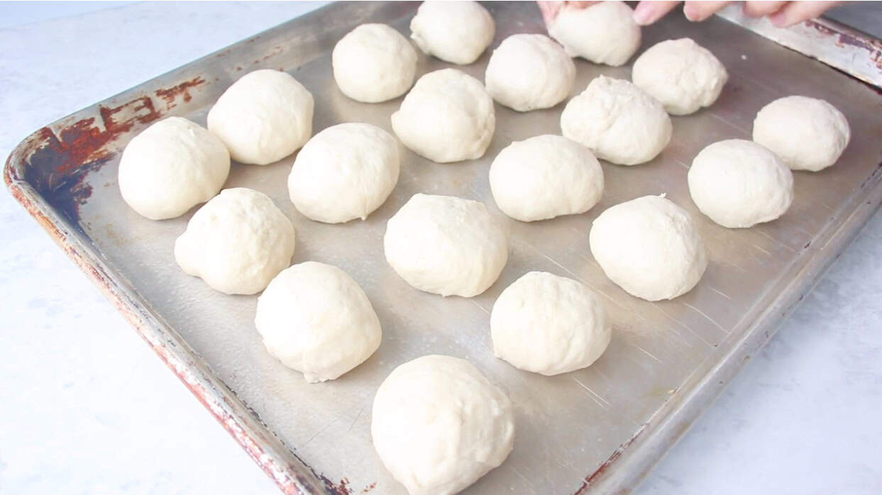 Metal baking sheet with balls of roll dough.
