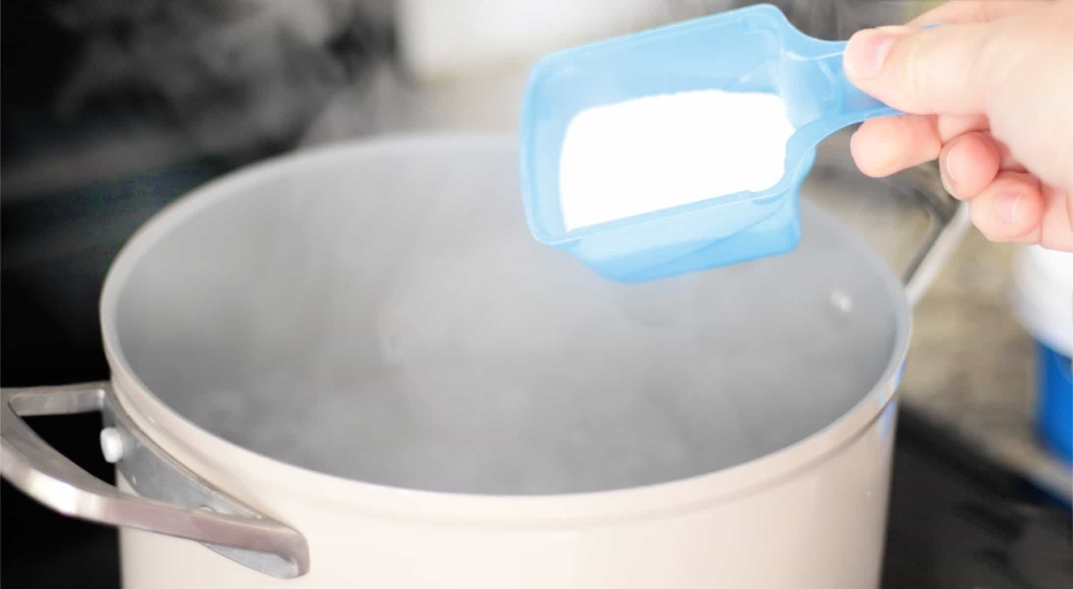 Pot of boiling water and scoop of Oxiclean powder in plastic scoop.