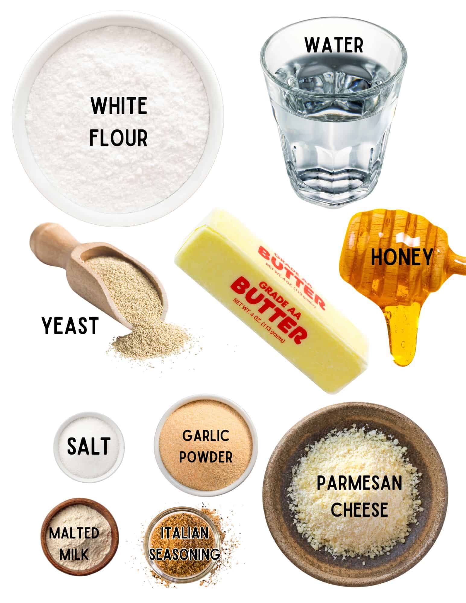 Bowls of flour, parmesan cheese, yeast, salt, dry milk, italian seasoning and garlic powder with glass of water, stick of butter and honey.