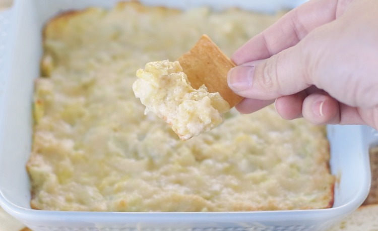 hand holding pita chip dipped in artichoke dip