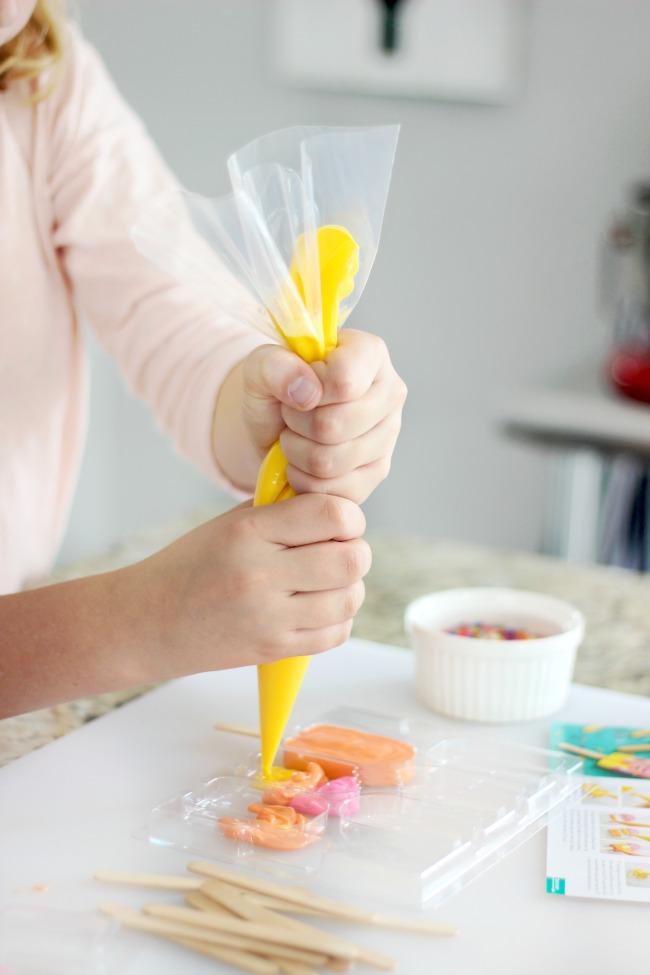 child piping melting candies into popsicle mold