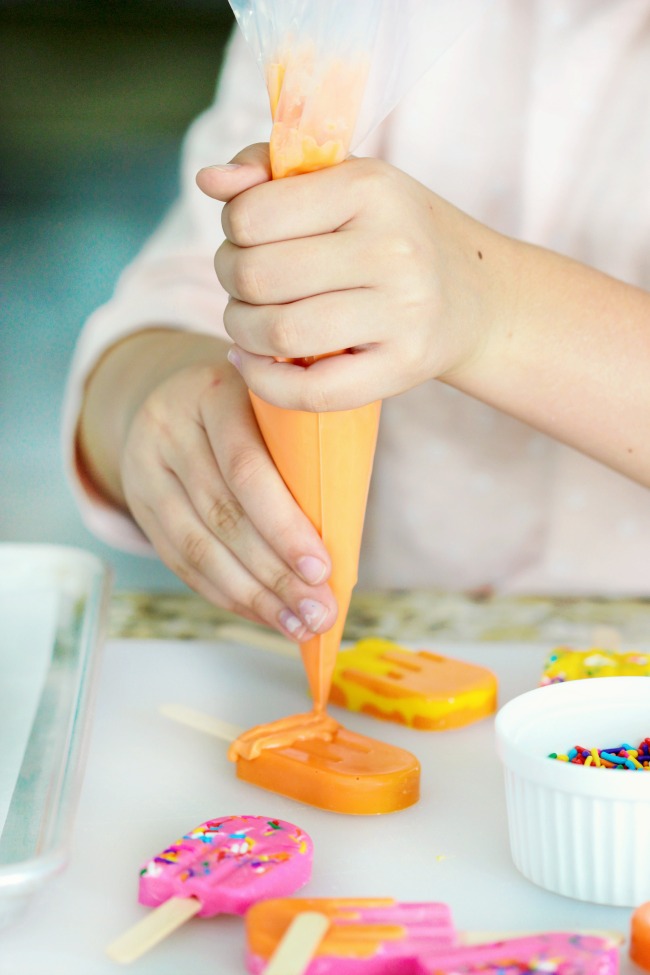 child adding sprinkles to candy popsicle