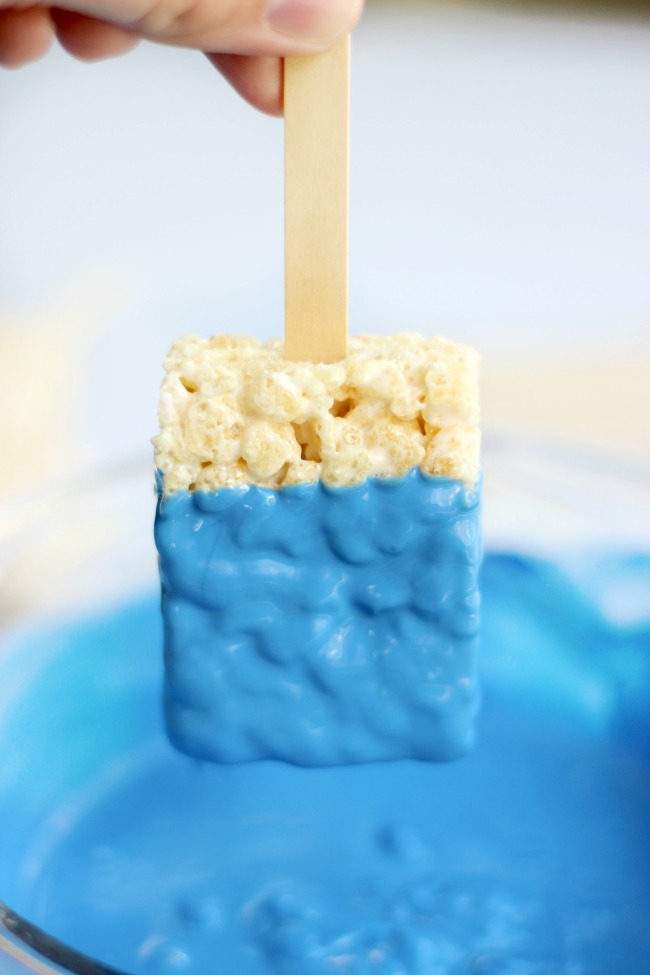 dipping rice krispies treat into blue melted chocolate