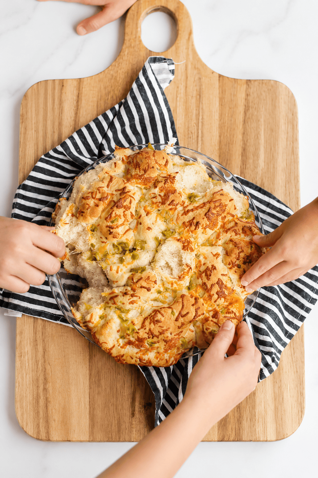 Hands pulling piece of jalapeno cheese bread from loaf.
