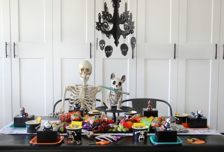 table with skeletons, party supplies, black table cloth and chandalier (finished party)