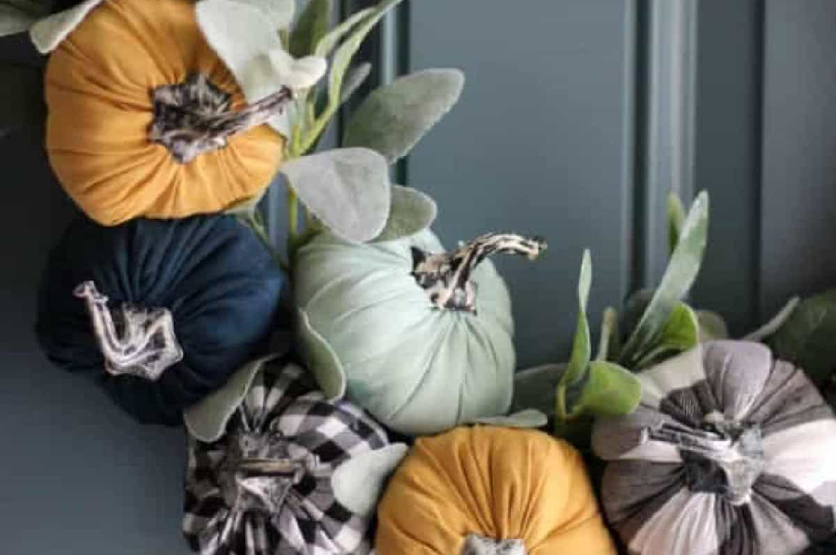 Wreath hanging on door with greenery tucked in between pumpkins.