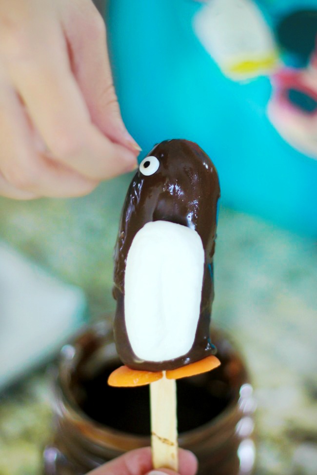 child adding candy eyes to banana penguin edible craft