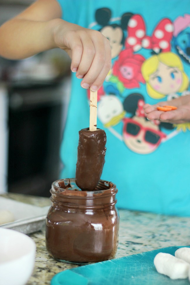 child dipping banana into melting chocolate