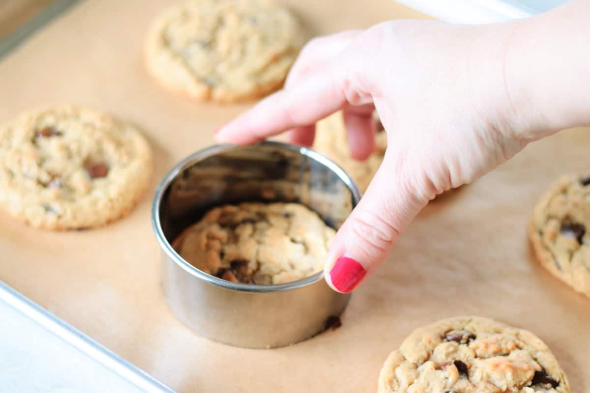 Round metal cookie cutter reshaping hot cookies on baking sheet.