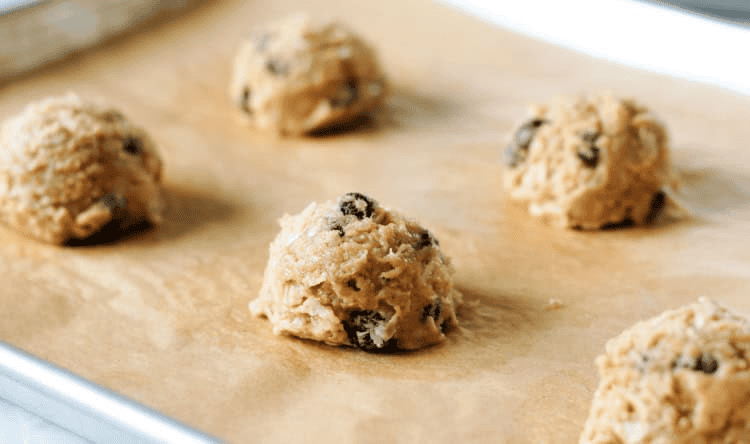 Balls of chocolate chip oatmeal cookie dough on parchment paper lined baking sheet.