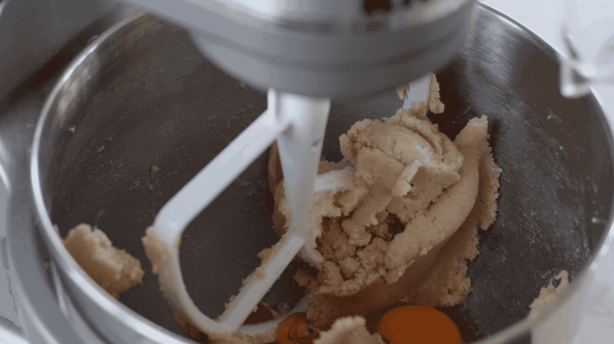 Metal stand mixer bowl with eggs, but and sugar.