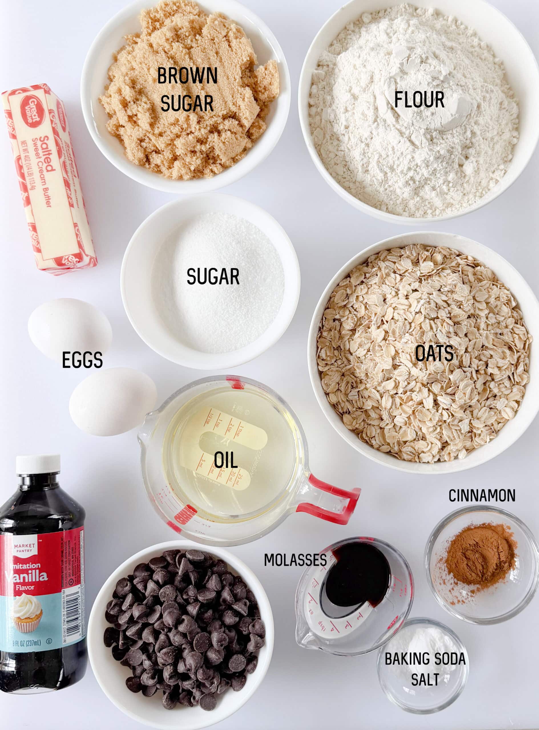 Bowls of brown sugar, white sugar, oats, stick of butter, chocolate chips, bottle of vanilla, two eggs, cup of oil, molasses, cinnamon, baking soda and salt.