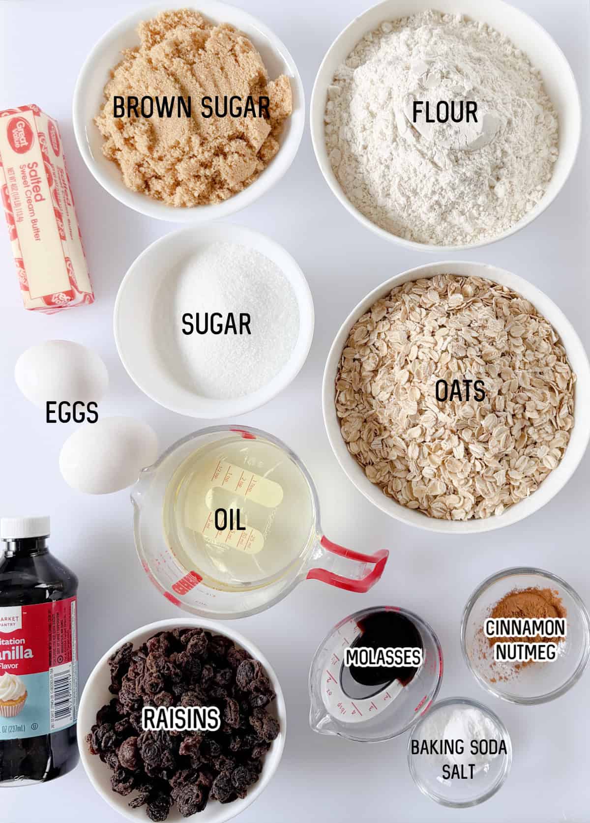Bowls of brown sugar, white sugar, oats, stick of butter, raisins, bottle of vanilla, two eggs, cup of oil, molasses, cinnamon, baking soda and salt.