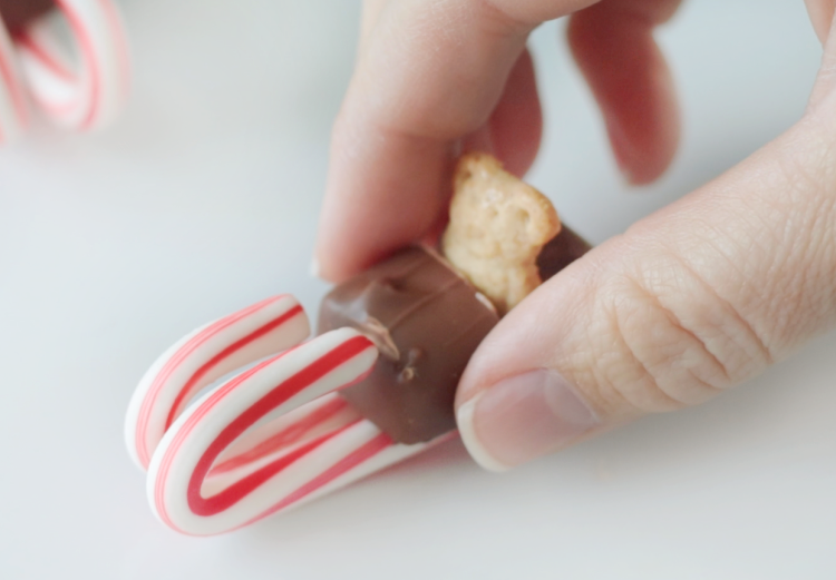 fingers placing candy bar on candy canes with frosting
