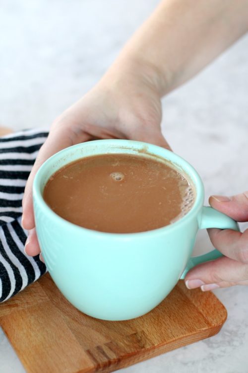 hands holding teal mug of cocoa