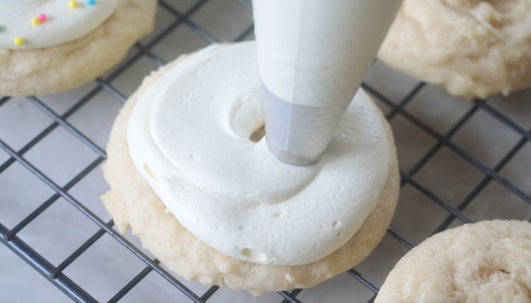 frosting being piped on sugar cookies