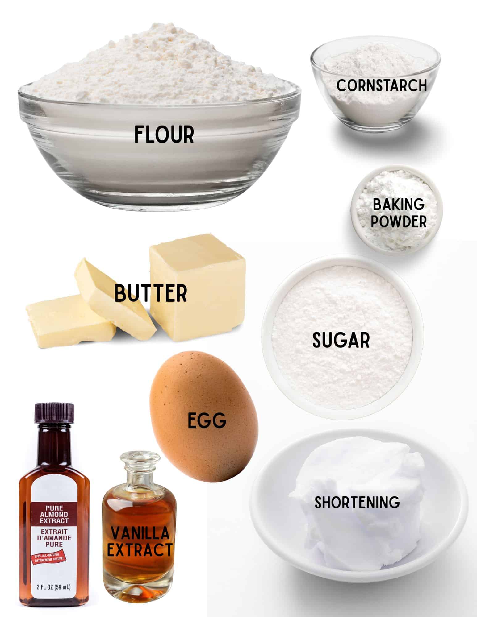 Bowls of flour, cornstarch, baking pwder, and shortening, with stick of butter, egg, and bottles of vanilla and almond extract.