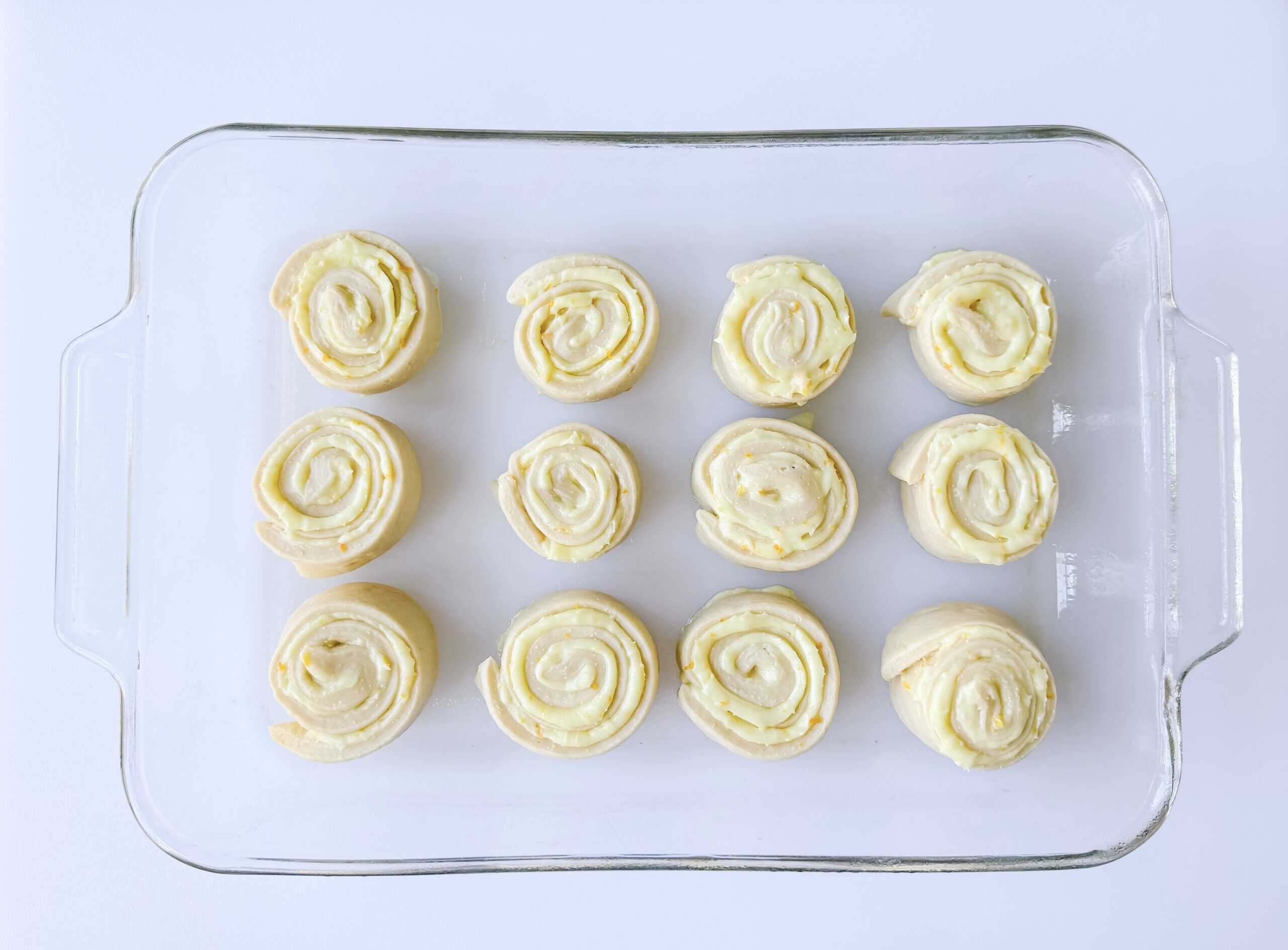 Glass baking dish of unbaked orange rolls.