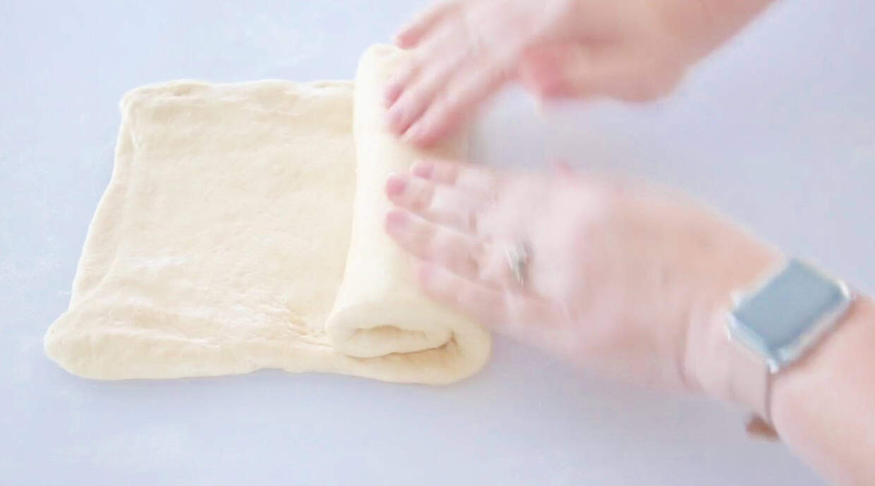 Hands rolling bread dough into a loaf.
