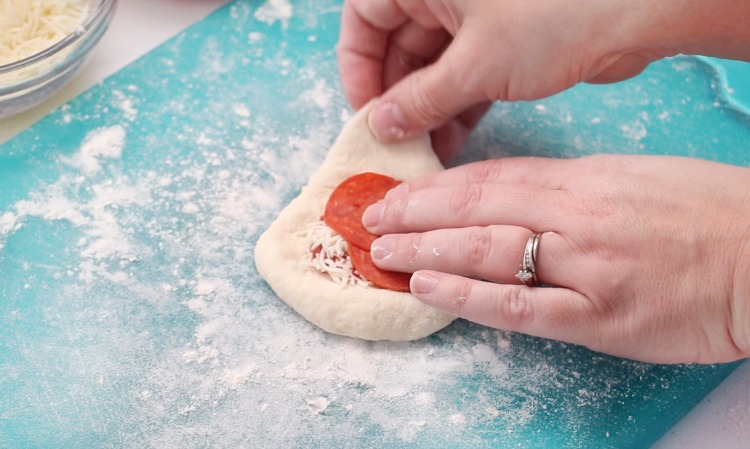 pizza dough spread out with sauce, cheese and 2 pepperoni pieces