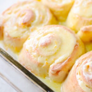Baked and frosted orange rolls in baking dish.