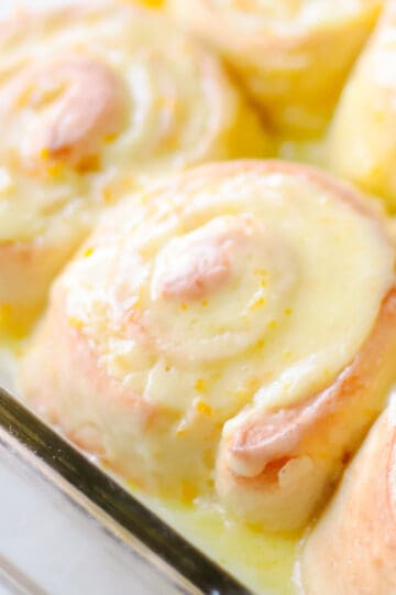 Baked and frosted orange rolls in baking dish.