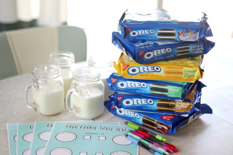 table with stack of oreo packages, pens, printable worksheets and glasses of milk