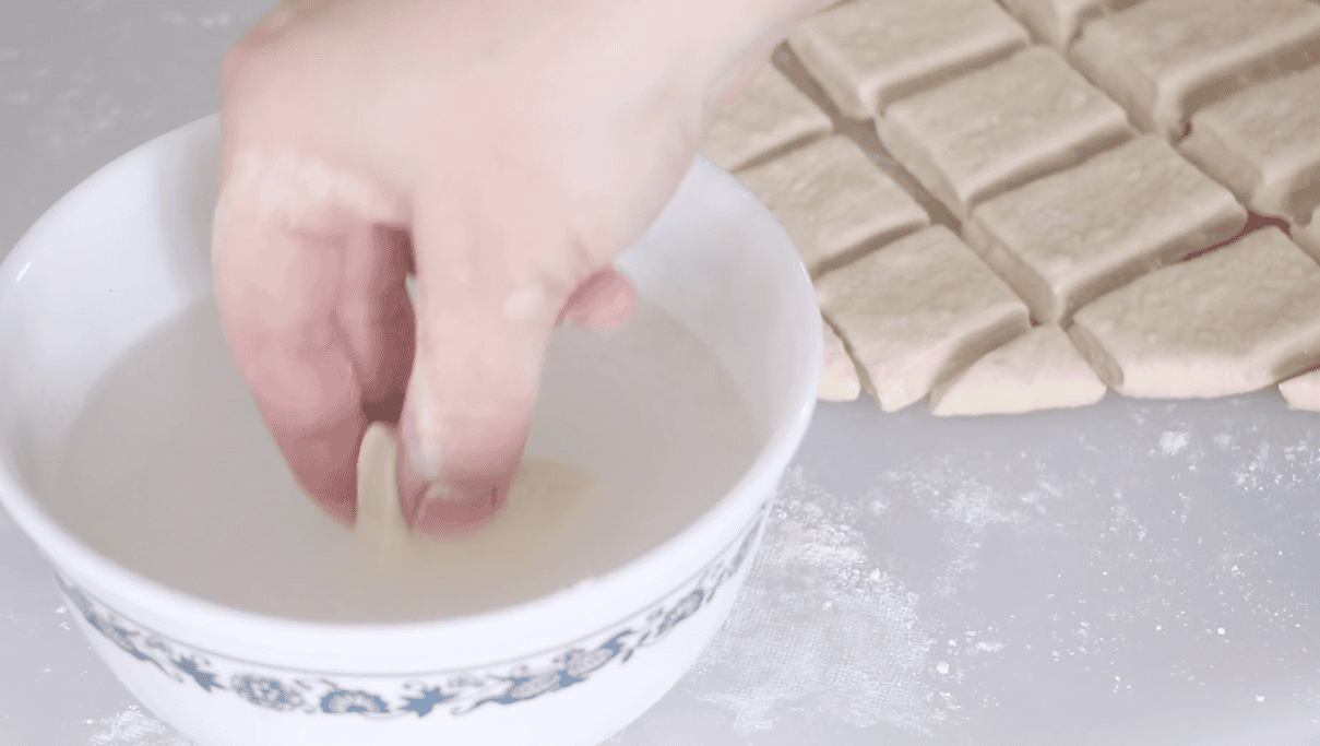 Hand dipping unbaked pretzel bites in baking soda bath.