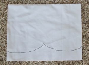 white fabric with a black line drawn to show how to cut scalloped edge