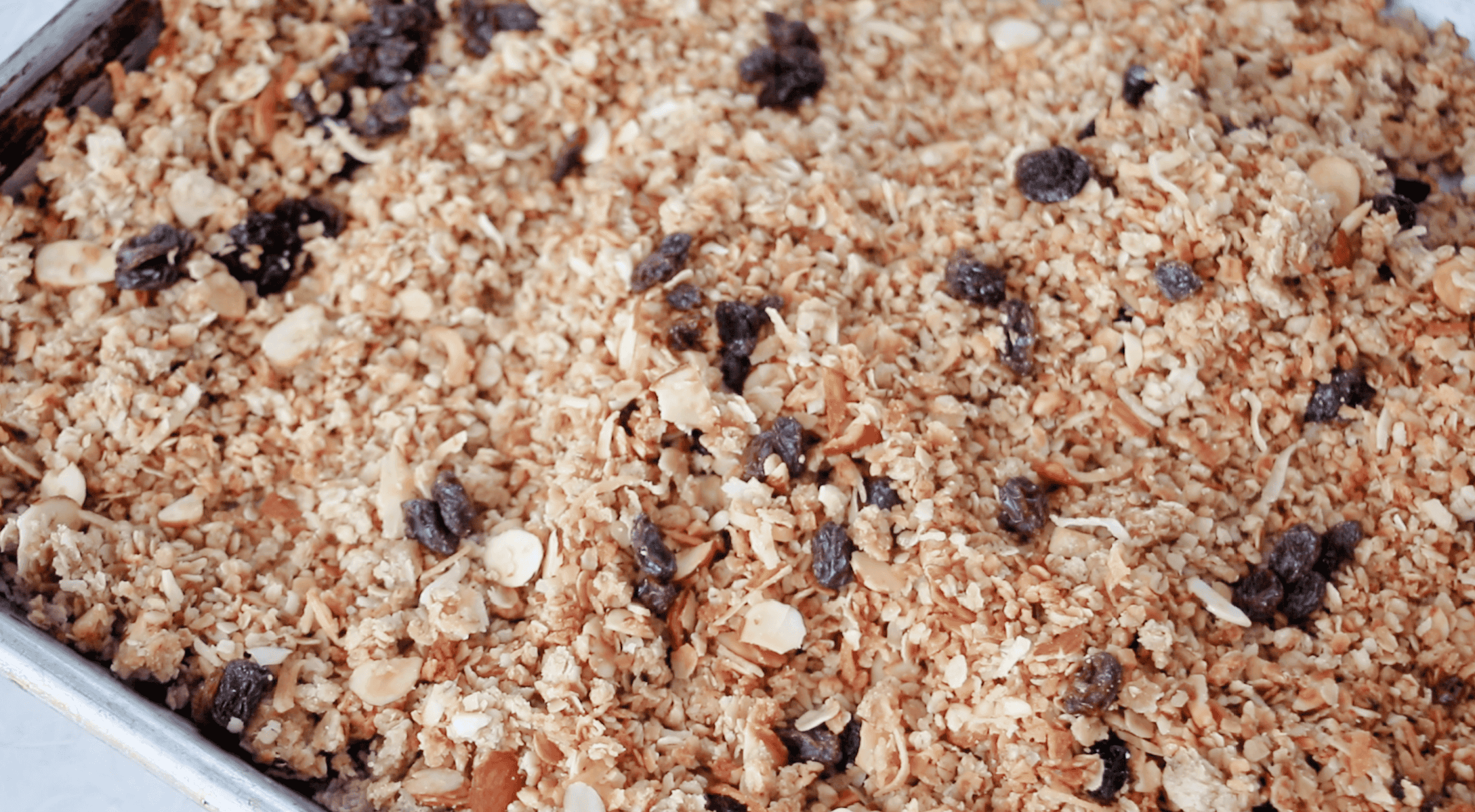 Baked granola with raisins on large baking sheet.
