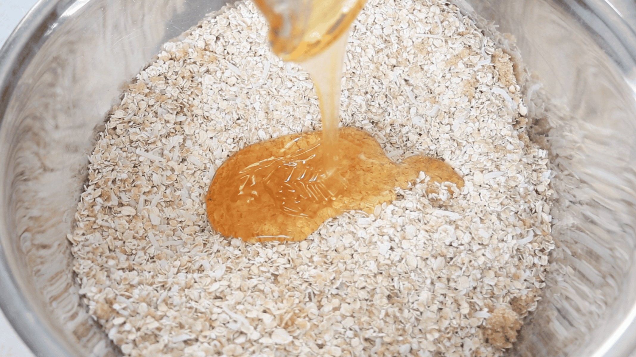 Large metal bowl with oat mixture and honey being poured on top.