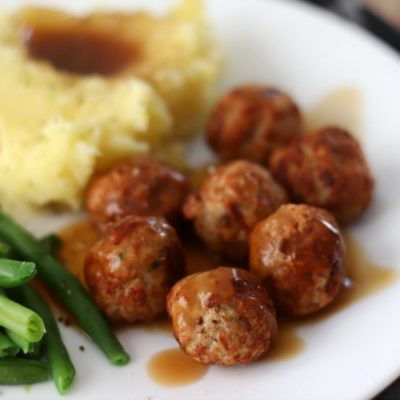 meatballs on white plate with sauce, green beans and mashed potatoes