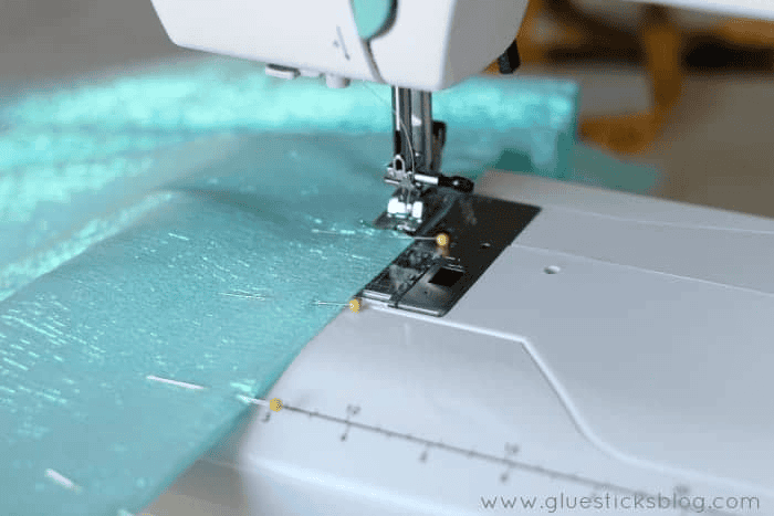 Blue sparkly fabric being sewn with sewing machine.