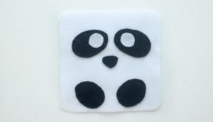 white square of felt with black ovals of felt for eyes and feet