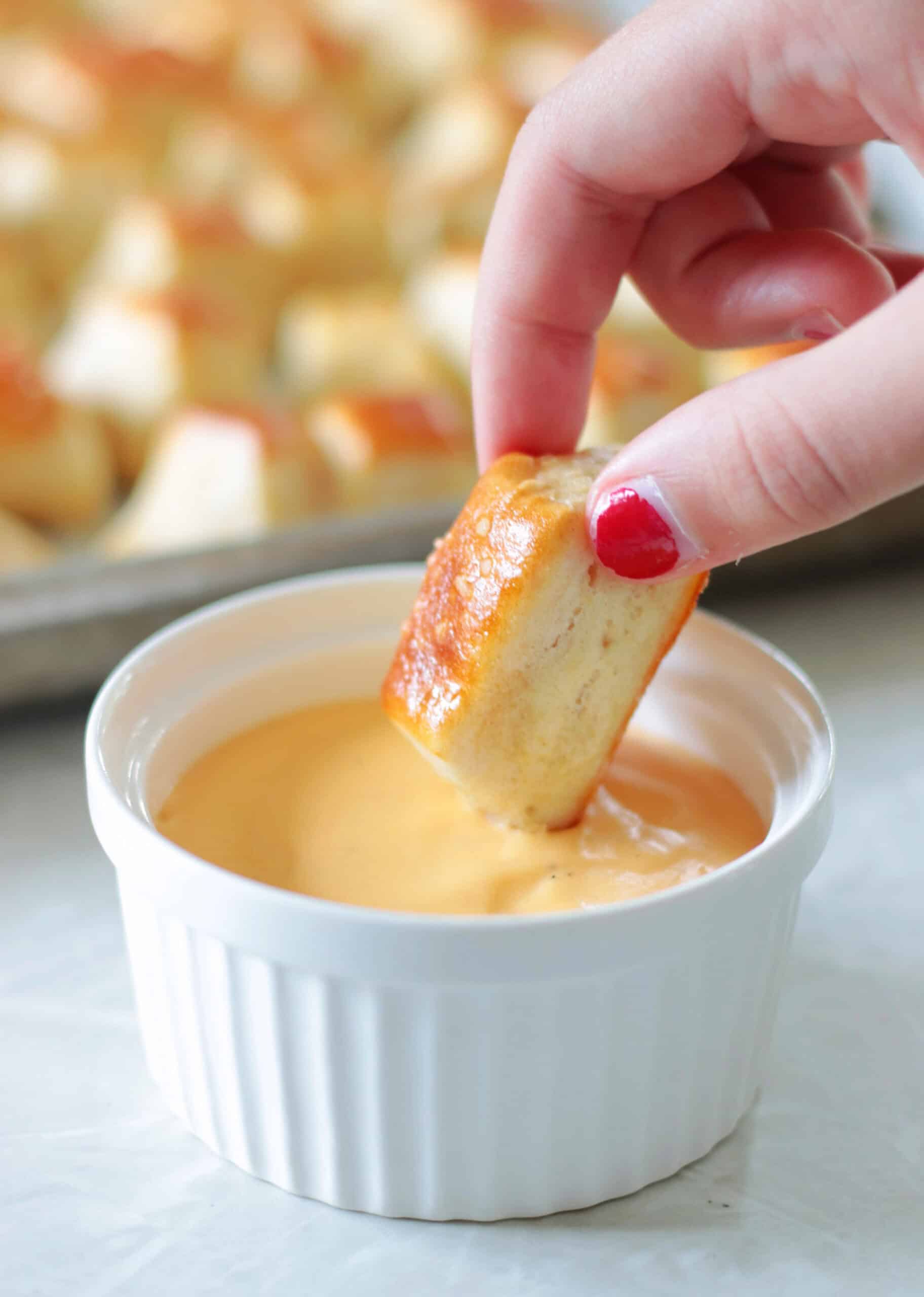 Hand dipping pretzel bite into cheese sauce.
