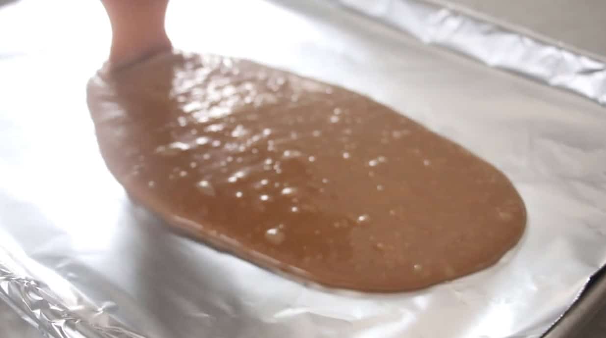 Hot toffee being poured onto baking sheet lined with foil.