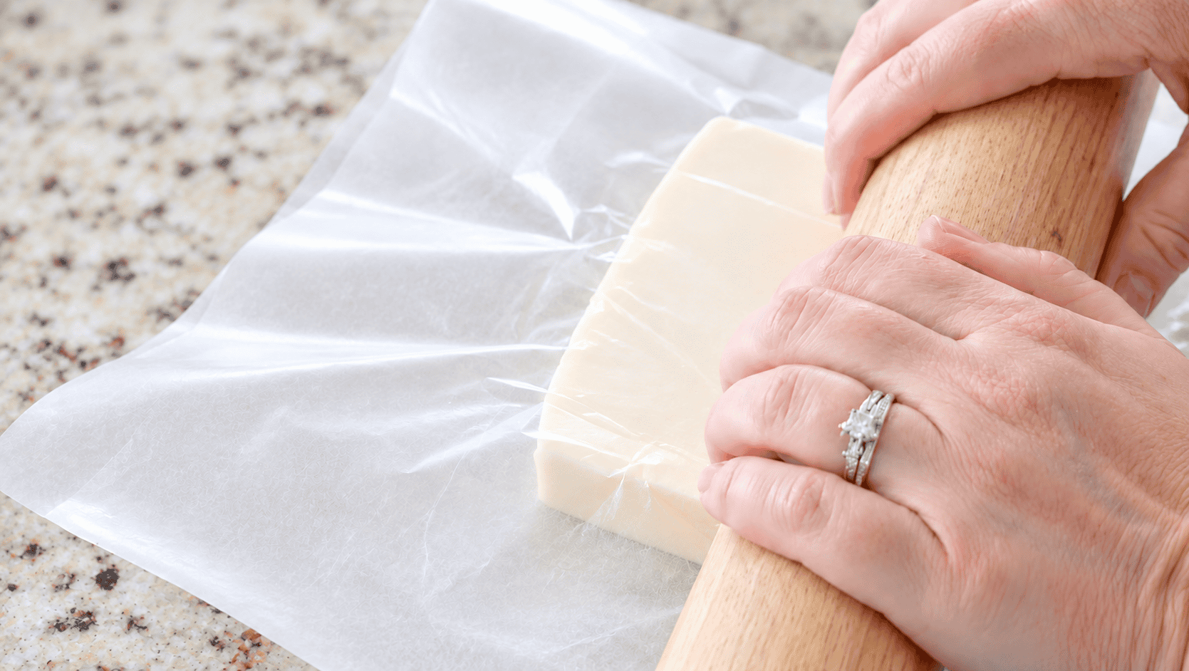 Hand rolling out butter with rolling pin between wax paper.