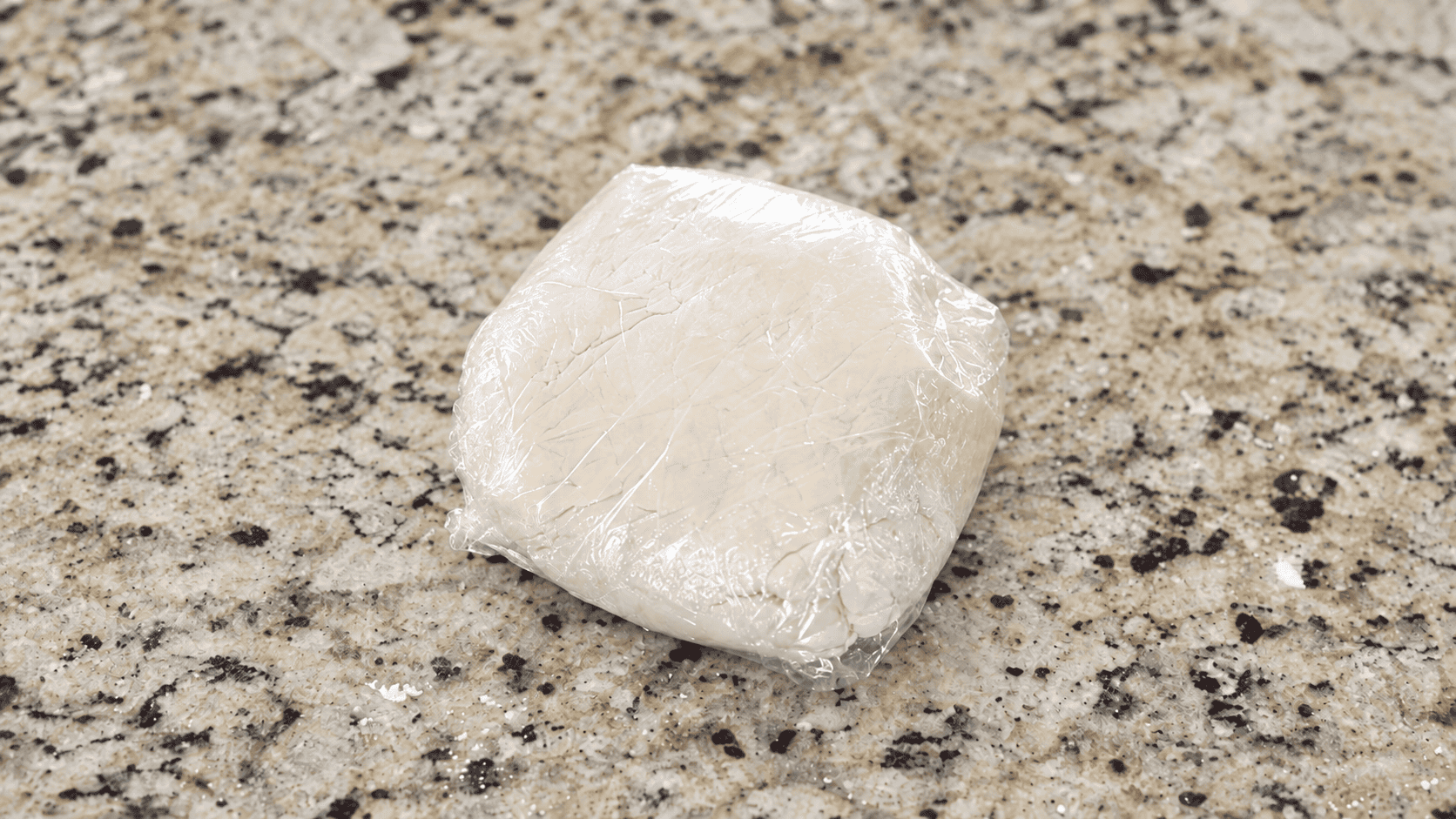Dough wrapped in plastic wrap on counter top.