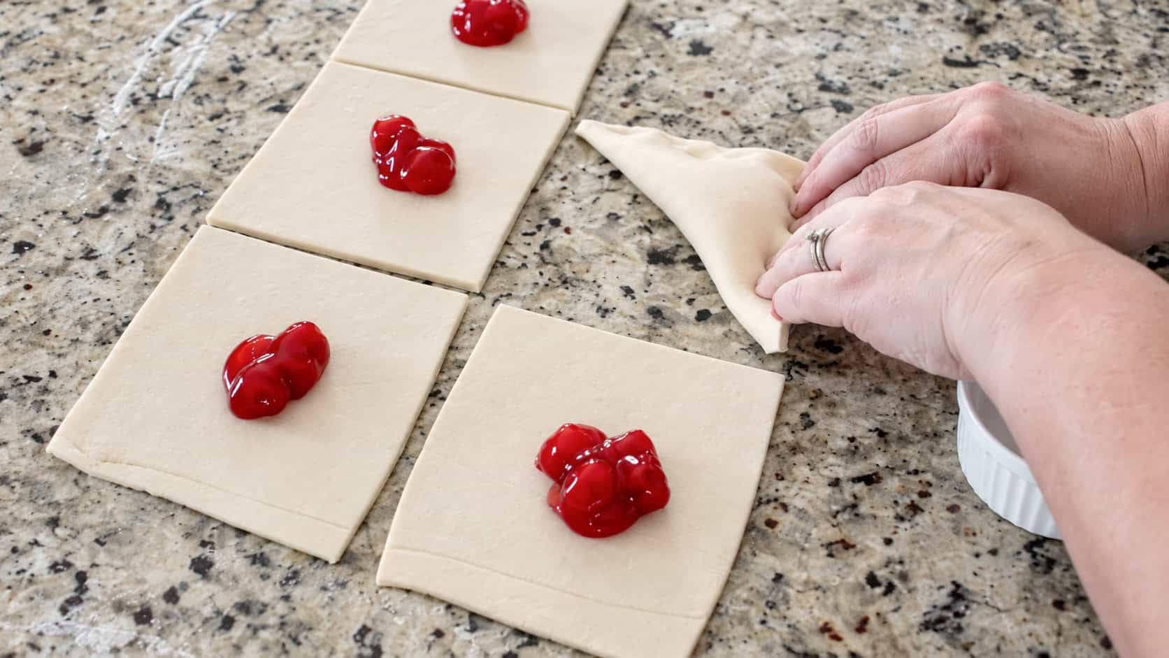Squares of puff pastry dough with spoonfuls of cherry pie filling in the center of each.