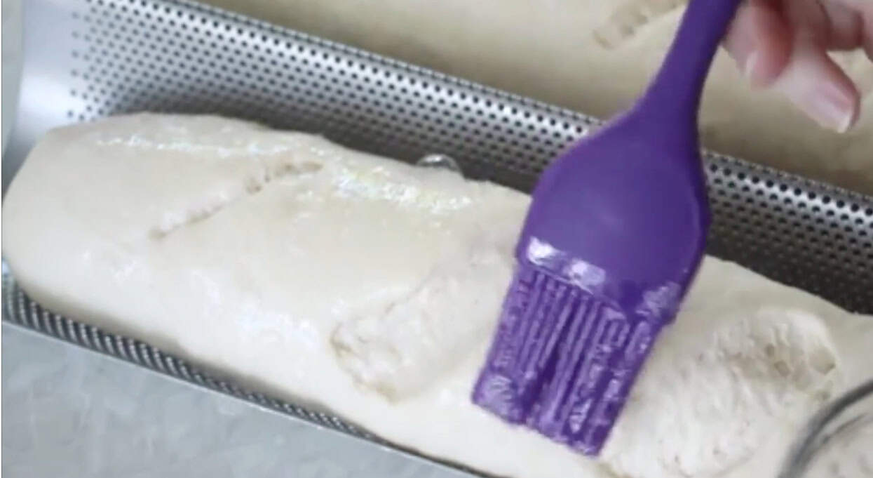 Pastry brush brushing egg wash over unbaked loaves.