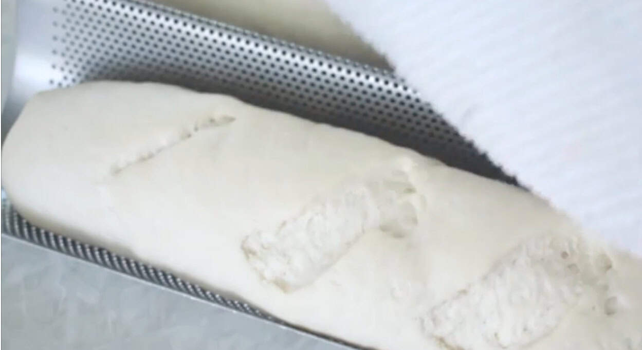 Loaf of unbaked French bread in metal pan.