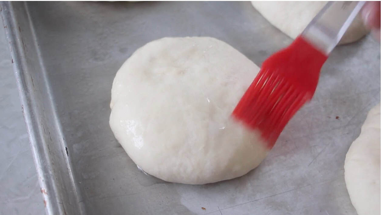 Pastry brush brushing egg onto unbaked hamburger buns.