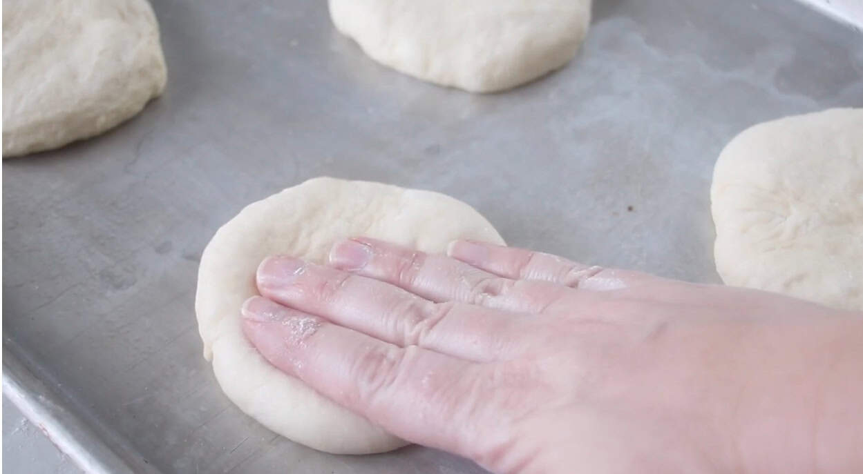 Hand pressing down on unbaked buns to flatten.