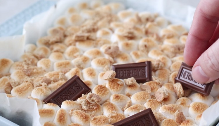 hand placing pieces of chocolate bar on top of toasted marshmallows