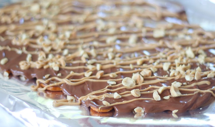 toffee on baking sheet drizzled in peanut butter and sprinkled with peanuts