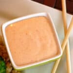 Square bowl of yum yum sauce on plate with chop sticks.